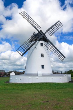 Windmill close up, black slatted sails, black roof, white render and blue cload sky