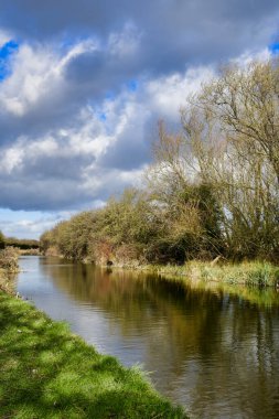 Slow flowing river, canal in winter, tree lined with stormy sky