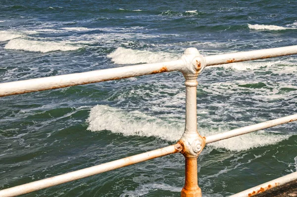 Ocean Waves through iron rusting safety railings, blue, green water and white caps