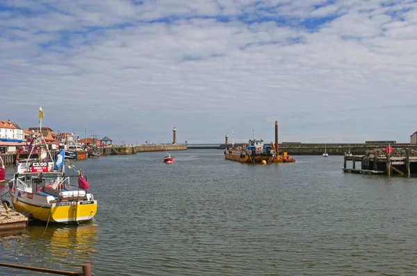 Whitby, United Kingdom - July 13, 2016: Whitby Harbour, Charter fishing boat tied up at dock, River Esk, Whitby North Yorkshire. Dredger in mid river with the harbour piers in distance.