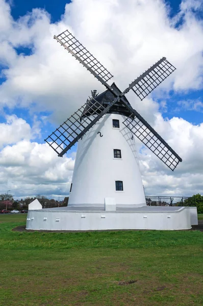Windmill close up, black slatted sails, black roof, white render and blue cload sky