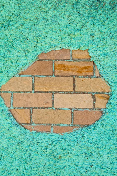 Exposed pale bricks surrounded by aquamarine pebbles in cement