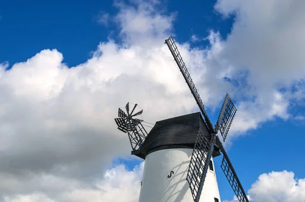 Windmill close up, black slatted sails, black roof, white render and blue cload sky