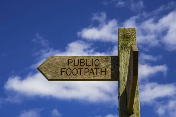 Wooden public footpath sign, isolated against blue sky with white clouds