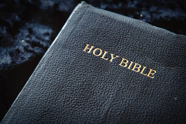 Close up of Holy Bible front cover, shallow depth of field, with focus on gold wording, dark blue, black and worn from years of use