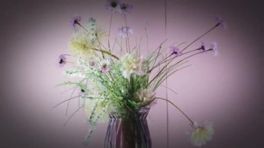 Bir buket pembe gerbera ve diğer çiçekleri içeren dönen vazo renkli bir arka plana karşı dizilmiş.