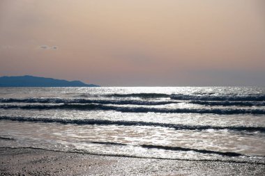 Fırtınalı deniz dalgaları öğleden sonra geç saatlerde Kıbrıs 'taki Ayia Eirini' de kumlu bir sahile vurdu. Uzakta Troodos dağları belirir.
