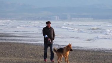 Ayia Eirini, Kıbrıs - 20 Mart 2022: Köpekli bir adam ve diğer insanlar fırtınalı bir öğleden sonra Kıbrıs Rum Kesimi 'nin Ayia Eirini plajında deniz dalgaları sahile vururken.