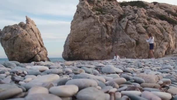 一名妇女在塞浦路斯帕福斯Petra Tou Romiou岩石海滩为另一名妇女拍照 海滩被认为是阿芙罗狄蒂在希腊神话中的诞生地 — 图库视频影像