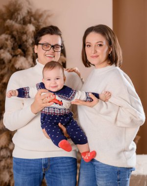 Genç aile babası anne oğul kışın giydiği bej renklerle Noel ağacı dekoru üzerinde yürüyorlar.