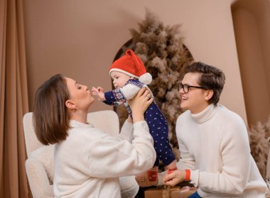 Genç aile babası anne oğul kışın giydiği bej renklerle Noel ağacı dekoru üzerinde yürüyorlar.