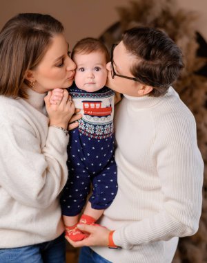 Genç aile babası anne oğul kışın giydiği bej renklerle Noel ağacı dekoru üzerinde yürüyorlar.