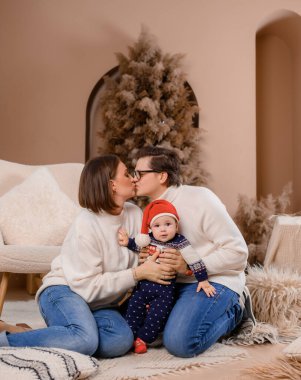 Genç aile babası anne oğul kışın giydiği bej renklerle Noel ağacı dekoru üzerinde yürüyorlar.