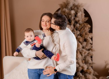 Genç aile babası anne oğul kışın giydiği bej renklerle Noel ağacı dekoru üzerinde yürüyorlar.