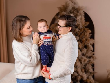 Genç aile babası anne oğul kışın giydiği bej renklerle Noel ağacı dekoru üzerinde yürüyorlar.