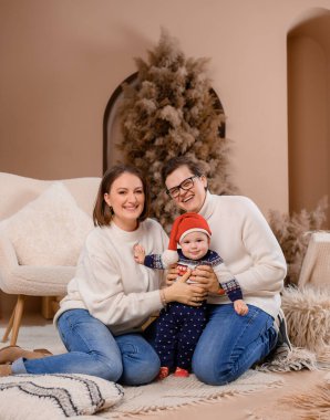 Genç aile babası anne oğul kışın giydiği bej renklerle Noel ağacı dekoru üzerinde yürüyorlar.