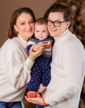 Genç aile babası anne oğul kışın giydiği bej renklerle Noel ağacı dekoru üzerinde yürüyorlar.