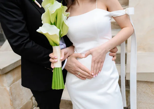 Красива молода пара наречених позує роблячи руки серцем на животі вагітної нареченої — стокове фото