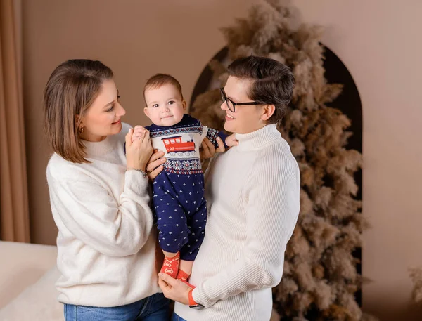 Genç aile babası anne oğul kışın giydiği bej renklerle Noel ağacı dekoru üzerinde yürüyorlar.