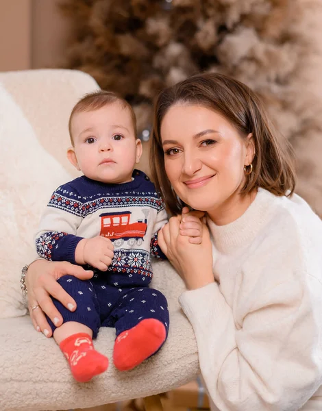 Genç aile annesi ve oğlu yeni yıl ağacının arka planında poz veriyorlar.