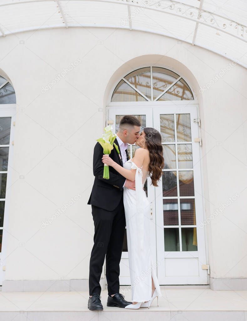 Beautiful young newlyweds couple kiss on the background of a beautiful building