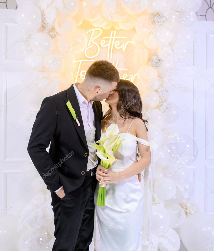 Beautiful newlywed couple posing on a background of photo decor with white balloons
