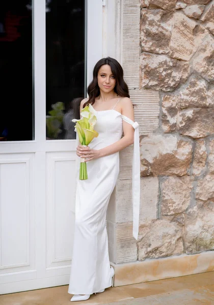 Красивая невеста позирует на фоне окна со свадебным букетом — стоковое фото