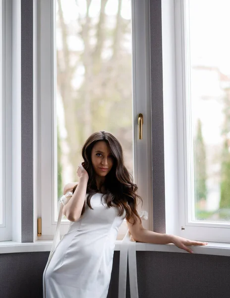 Beautiful bride posing on the background of a window with a wedding bouquet — Fotografia de Stock