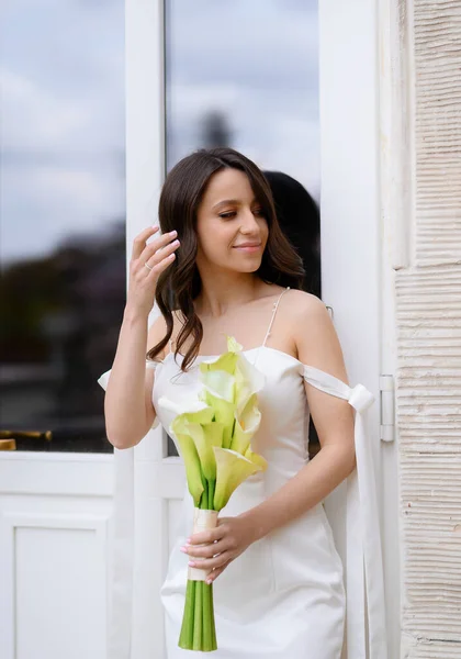 Beautiful bride posing on the background of a window with a wedding bouquet — стоковое фото