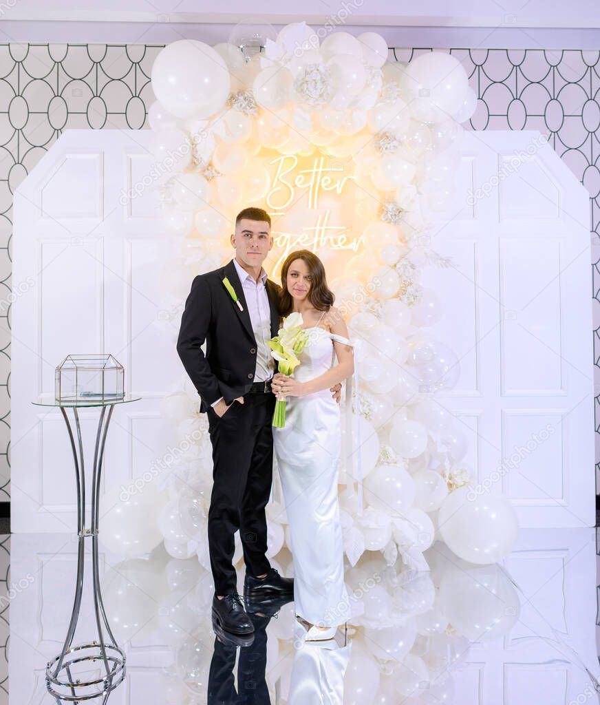 Beautiful newlywed couple posing on a background of photo decor with white balloons