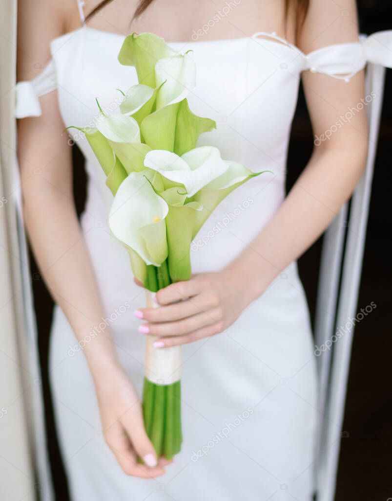 Beautiful young bride posing with a bouquet in her hands by the window