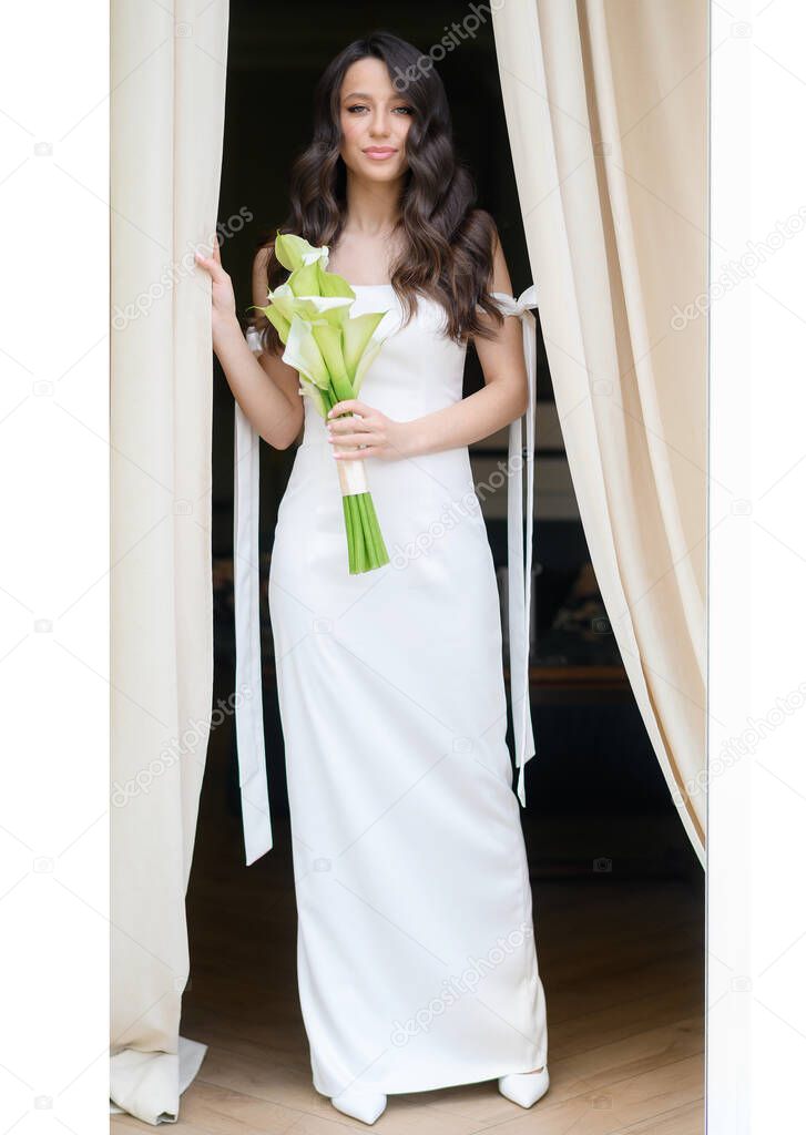 Beautiful young bride posing with a bouquet in her hands by the window