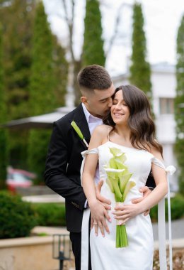 Beautiful young newlyweds couple embracing on the background of a beautiful building