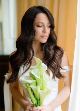 Pencere kenarında elinde buketle poz veren güzel bir gelin.