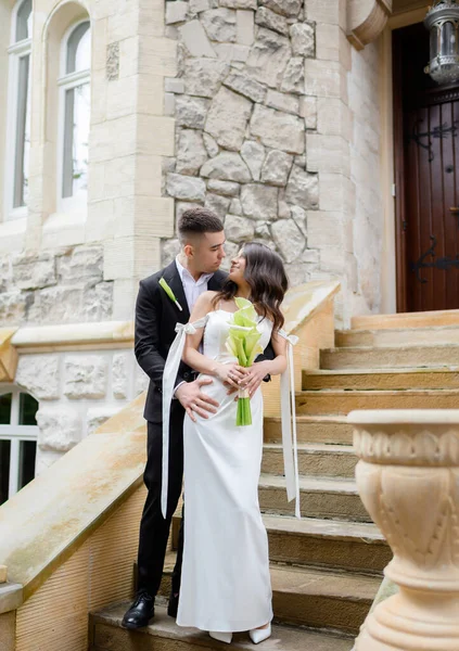 Bela jovem casal recém-casado posando no fundo de um edifício antigo — Fotografia de Stock