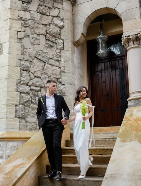 Bela jovem casal recém-casado posando no fundo de um edifício antigo — Fotografia de Stock