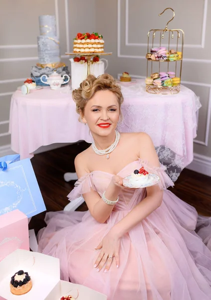 Güzel sarışın kadın pembe elbiseli bir pasta tutuyor.