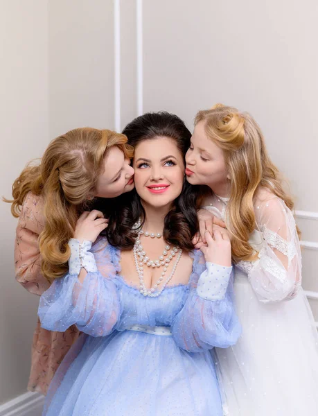 İki genç sarışın kız annelerine sarılıp öpüşüyorlar.