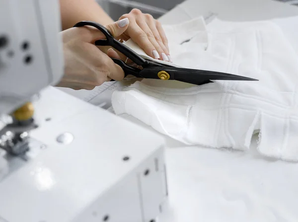 Young beautiful blonde hair seamstress cuts the fabric in the workplace. — Fotografia de Stock