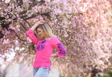 Güzel sarı saçlı kız çiçek açan sakura ağacının arka planında duruyor.