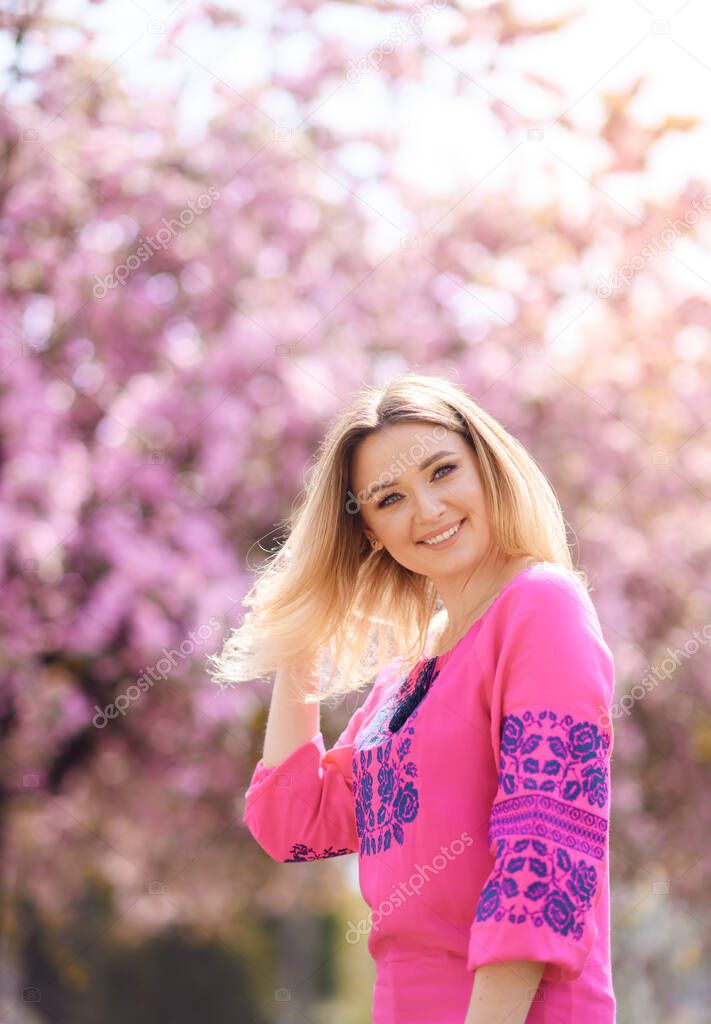 Beautiful blonde hair girl stands on a background of blooming sakura tree
