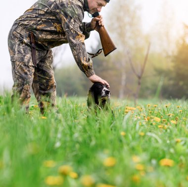 Omzunda silahla bir erkek avcısı Rus bir köpeği okşuyor.
