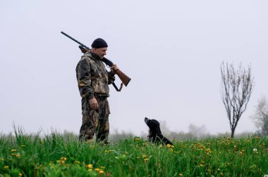 Omzunda silah olan bir erkek avcısı Rus bir köpekle duruyor. 