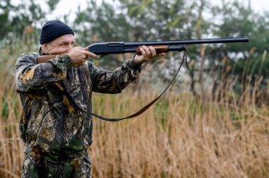 Silahlı bir erkek avcı sazlıkların arka planına nişan alır.