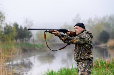 Tüfekli bir erkek avcı gölün arka planına nişan alır.