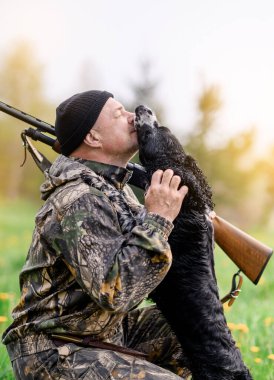 Omzunda silah olan bir erkek avcı Rus bir köpeğe sarılıyor.