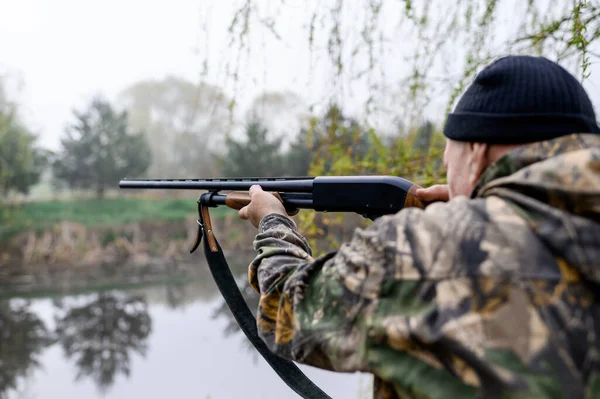 A male hunter with a rifle hunts and aims against the background of lake — Stockfoto