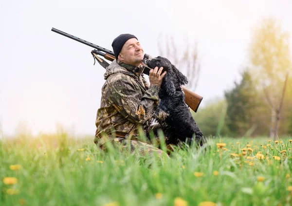 Male hunter with a gun on his shoulder hugging a Russian spaniel dog — Stockfoto
