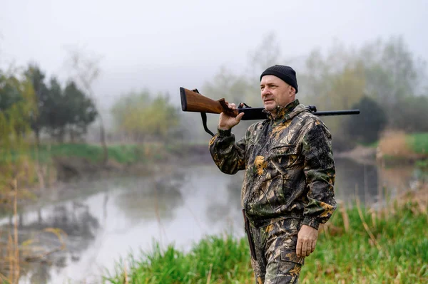 A handsome man with a gun on his shoulder looks at the lake in the fog — Stockfoto