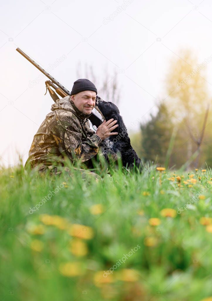 Male hunter with a gun on his shoulder hugging a Russian spaniel dog